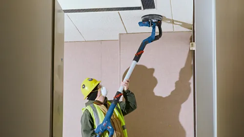 Persona usando equipo de seguridad utilizando una lijadora Bosch en un techo.