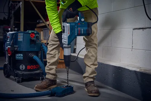 Taladro percutor Bosch 11264EVS utilizado para perforar una superficie, con aspiradora HEPA Ready y accesorio de recolección de polvo.