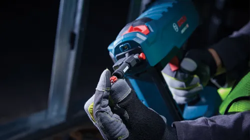 Herramienta Bosch, con logotipo "BOSCH" visible, en uso por persona que lleva guantes de trabajo y un chaleco de alta visibilidad.