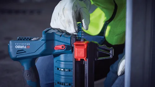 Herramienta BRUSHLESS BiTURBO, roja y verde azulado, con una mano enguantada y un chaleco de alta visibilidad.