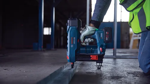 Bosch GNB18V-12 HD Turbo clavadora sin escobillas siendo utilizada por una persona, clavadora fijada a una viga metálica. La clavadora utiliza una batería de 18V.