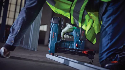 Bosch GNB18V-12 HD TURBO Clavadora inalámbrica sin escobillas, con "AMPshare" visible, sostenida por persona que lleva guantes y chaleco de seguridad.