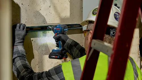 Persona que lleva guantes y equipo de seguridad utilizando un atornillador de impacto sin escobillas Bosch GDR18V-1860C.