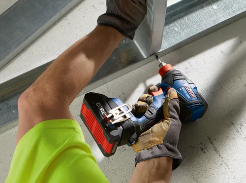 Persona con guantes utilizando un atornillador de impacto Bosch GDX18V-1800C para atornillar en una estructura metálica.