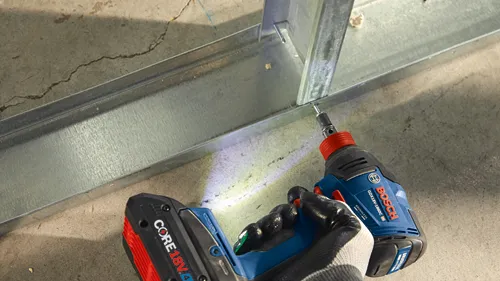 Atornillador de impacto Bosch GDX18V-1860C atornillando un tornillo en un perfil metálico, se ven manos con guantes de trabajo. Batería CORE18V 4.0 Ah conectada.
