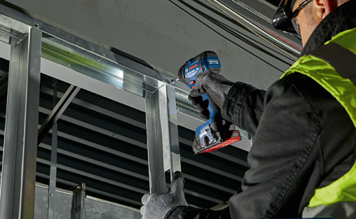 Destornillador de impacto Bosch GDR18V-1800 utilizado para fijar montantes metálicos; persona con gafas de seguridad y chaleco de alta visibilidad.