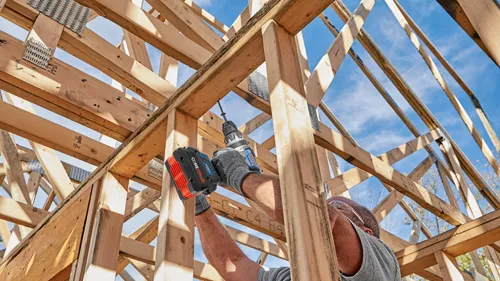 Una persona que utiliza un taladro inalámbrico Bosch CORE18V 8.0Ah para ensamblar una estructura de marco de madera, usando gafas de seguridad.