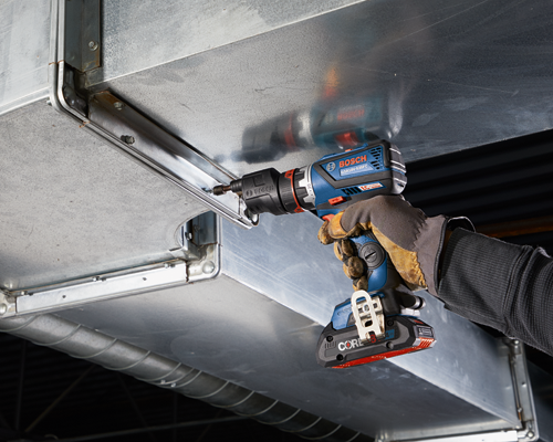 Bosch GSR18V-535FC taladro atornillador a batería utilizado para fijar un tornillo en una estructura metálica, sostenido por una persona que lleva guantes de trabajo.