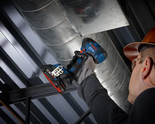 Destornillador de impacto a batería Bosch GDR18V-1800C utilizado para asegurar conductos metálicos; una persona que lleva guantes, tapones para los oídos y un casco de seguridad está utilizando la herramienta.