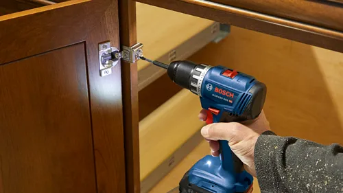 Bosch GSR18V-400 HD atornillando una bisagra en una puerta de armario.