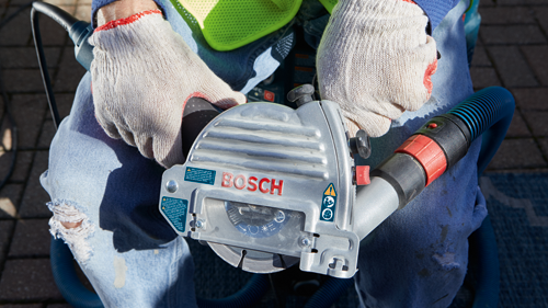 Amoladora Bosch con texto visible "BOSCH" e instrucciones de seguridad; sostenida por persona que lleva guantes.