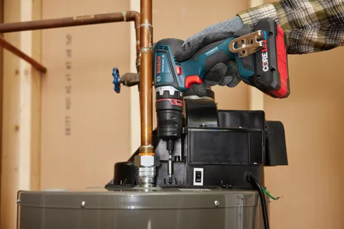 Taladro Bosch GSR18V-900FC con KICKBACK CONTROL sostenido por una persona que lleva una camisa a cuadros y guantes de trabajo sobre un calentador de agua, con un interruptor ON/OFF.