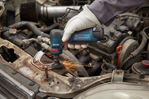 Herramienta con motor sin escobillas Bosch GWG12V-20S utilizada para cortar metal cerca del motor de un automóvil, emitiendo chispas; incluye advertencia de seguridad.