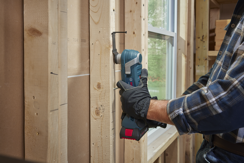 Herramienta multifunción oscilante Bosch StarlockPlus siendo utilizada por una persona que lleva una camisa a cuadros y guantes de trabajo cerca de una ventana.