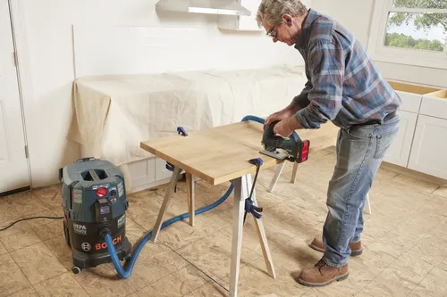 Un hombre cortando madera con una sierra de calar Bosch, conectada a una aspiradora Bosch HEPA Ready.