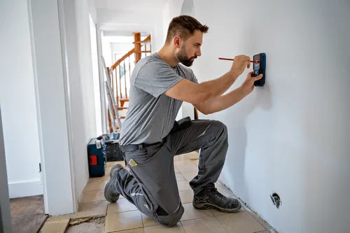 Persona arrodillada, usando un lápiz rojo para marcar una pared mientras sostiene una herramienta azul.
