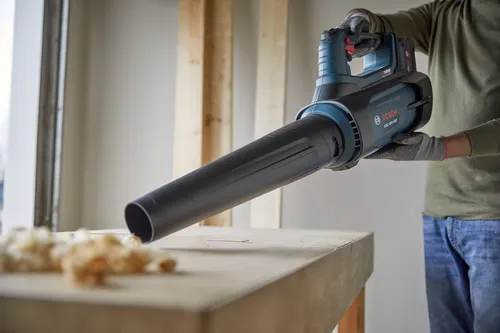 Soplador a batería Bosch GBL 18V-450 sujetado por una persona que lleva guantes y vaqueros.