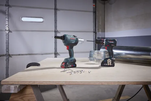 Bosch GRG18V-3600C y GSR18V-535FC taladros inalámbricos, baterías Core18V 4.0 y diversos componentes en una mesa de madera.