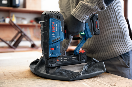 Clavadora Bosch GTH18V-18M, utilizada en material negro, por persona que lleva suéter gris y guantes.