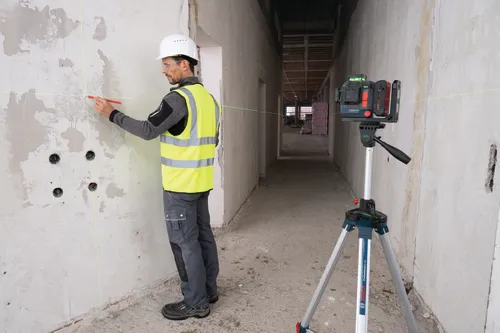 Una persona que lleva equipo de seguridad utiliza un bolígrafo rojo para marcar una pared mientras usa un trípode Bosch Professional GT 250 y un nivel láser Bosch.