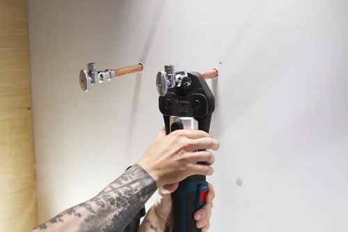 Crimpadora de tubos Bosch CUSS 1/2", utilizada para conectar tubos de cobre, con una persona sosteniéndola.