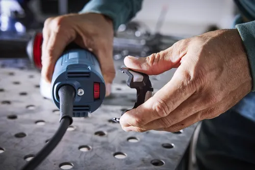 Persona sosteniendo una herramienta eléctrica y un componente pequeño, la herramienta tiene un dial rojo.