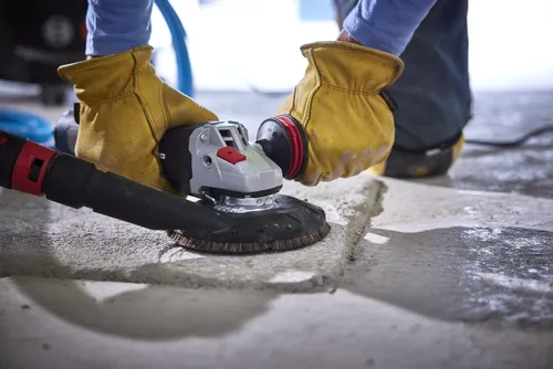Persona utilizando una amoladora eléctrica sobre una superficie de hormigón, con guantes amarillos.