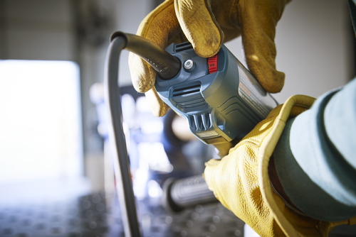 Herramienta eléctrica Bosch sostenida por una persona que lleva guantes de trabajo amarillos, con un interruptor rojo.