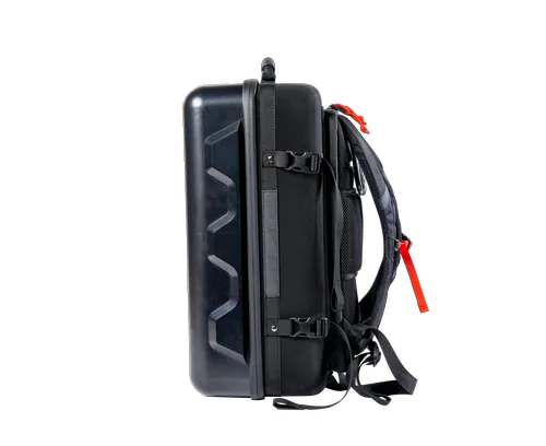 Maleta tipo mochila negra con correas, hebillas y asa rojas y negras. La maleta es rígida en un lado y parece ser de tela en el otro.