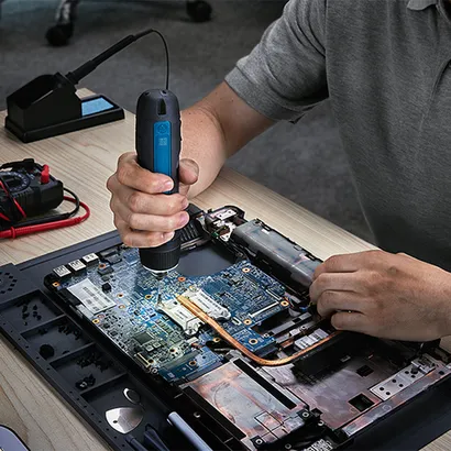 A technician sitting at a work bench using the Bosch GSD4V-35 rechargeable screwdriver repair a chip board of a device.