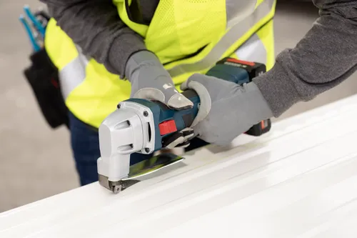 The worker using the Bosch GSC18V-16E 18V 16-Gauge Metal Shear with Lock- On Slide Switch to cutting a polycarbonate plate.