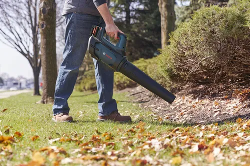 A worker using the Bosch GBL18V-450N PROFACTOR™ 18V Blower to blow the dry leaf from the garden.