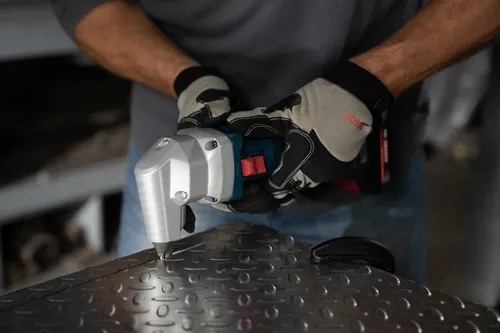 The worker using the GNA18V-16E 18V 16-Gauge Nibbler With Lock-On Slide Switch to cutting a corner of a metal table in a workshop.