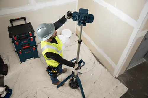 The worker using the Bosch GLT18V-5000N 18V Tower Light directed at a wall undergoing renovation for lighting purposes.