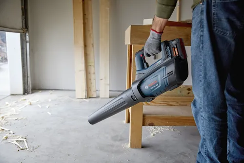 A worker using the Bosch GBL18V-450N PROFACTOR™ 18V Blower to blow wood sawdust on the floor.