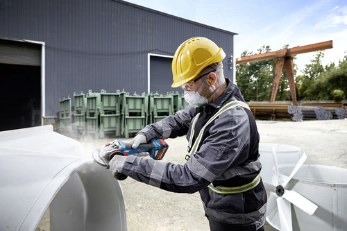 Trabajador utilizando una amoladora angular Bosch GWS18V-11S 18V sin escobillas de 4-1/2" a 5" para amolar el borde metálico de un ventilador industrial.
