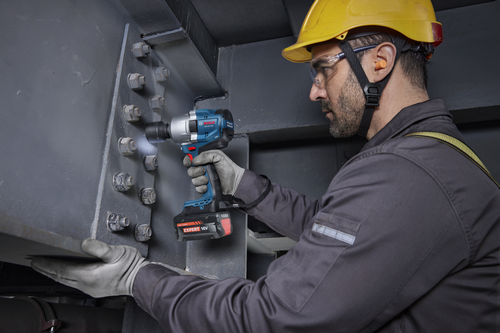 A worker using a Bosch GDS18V-780 18V Brushless Mid-Torque Impact Wrench to tighten bolts on a metal structure.