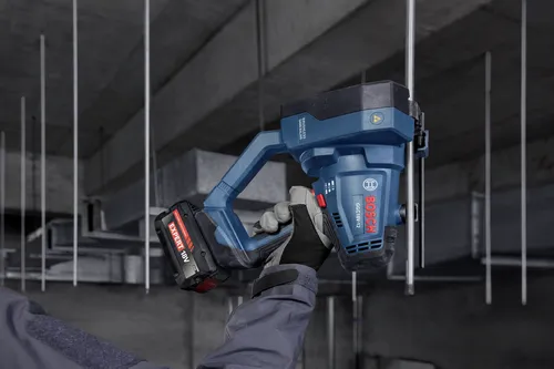 A worker using a Bosch GGC18V-12 18V Threaded Rod Cutter to cut through metal rods hanging from a concrete structure ceiling.