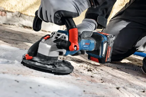 The close-up image of worker using the Bosch GBR18V-15S 5 In. 18V Concrete Surface Grinder to grind a hard concrete floor.