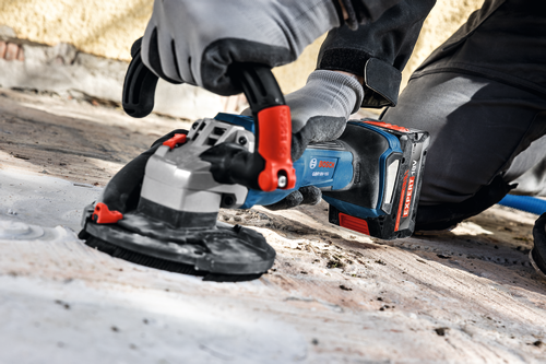The close-up image of worker using the Bosch GBR18V-15S 5 In. 18V Concrete Surface Grinder to grind a hard concrete floor.