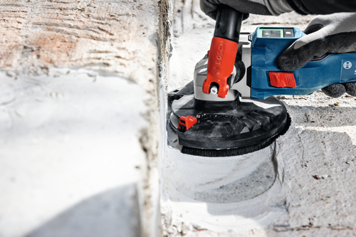 The close-up image of worker using the Bosch GBR18V-15S 5 In. 18V Concrete Surface Grinder to grind a hard concrete floor.