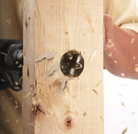 Perforación de un agujero en una tabla de madera con un taladro, con virutas de madera volando.
