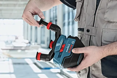 La herramienta de nivelación Bosch Professional GLL 3-50 es sostenida por una persona. La herramienta es negra y azul con detalles en rojo.